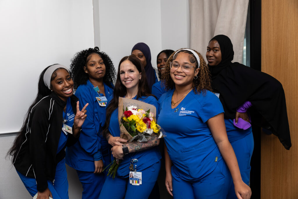 A group of Skills Initiative graduates smile and pose in their blue scrubs.