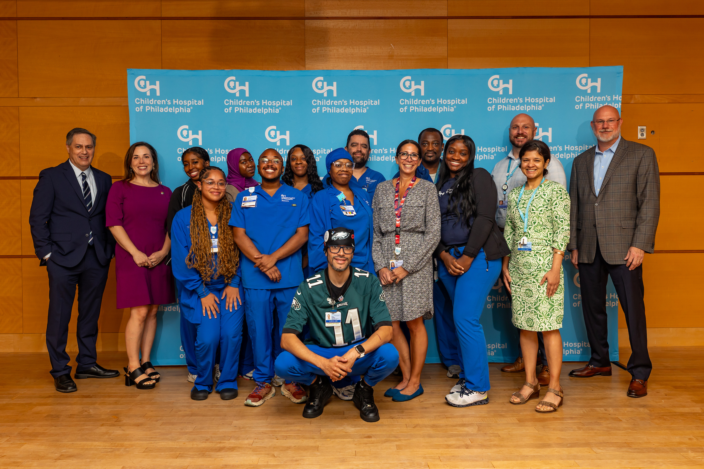 Smiling group of people standing in front of a photo background with the Children Hospital of Philadelphia logo